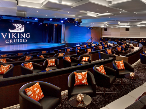 Interior of the Viking Star Theatre, with black chairs, orange throw pillows, and a stage with the Viking Logo in white.