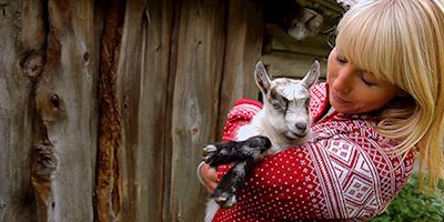 Karine Hagen in a red and white sweater, holding and hugging a baby goat to her chest.